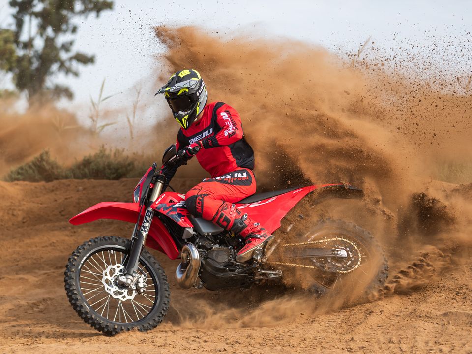 A Rieju rider in red kit throwing a wall of dirt from the rear wheel of a red MR 300i